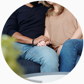 A couple sits with their hands held together on a sofa.